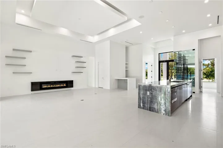 Kitchen featuring wall oven, light stone countertops, a center island with sink, a raised ceiling, and light tile floors
