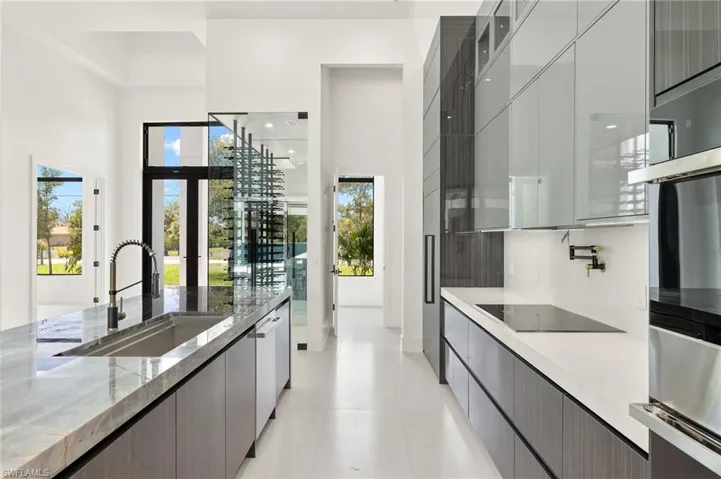Kitchen featuring light stone countertops, a towering ceiling, black electric cooktop, light tile floors, and sink