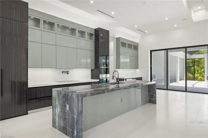 Kitchen with light tile flooring, gray cabinetry, a kitchen island with sink, dark stone countertops, and sink