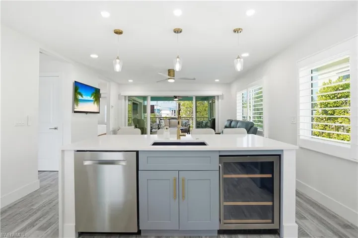 Kitchen featuring beverage cooler, dishwasher, an island with sink, open floor plan, and a ceiling fan - Virtually Edited Image