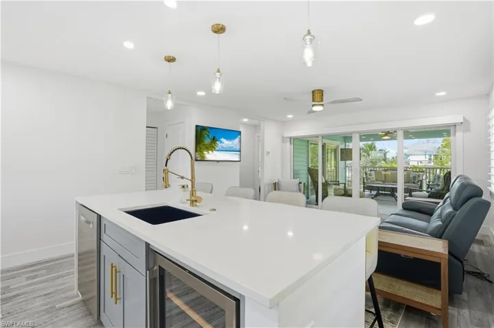 Kitchen with light wood finished floors, beverage cooler, hanging light fixtures, open floor plan, and light stone countertops - Virtually Edited Image