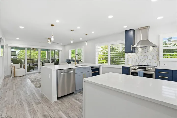 Kitchen with ceiling fan, light stone counters, decorative light fixtures, stainless steel appliances, and a center island with sink - Virtually Edited Image