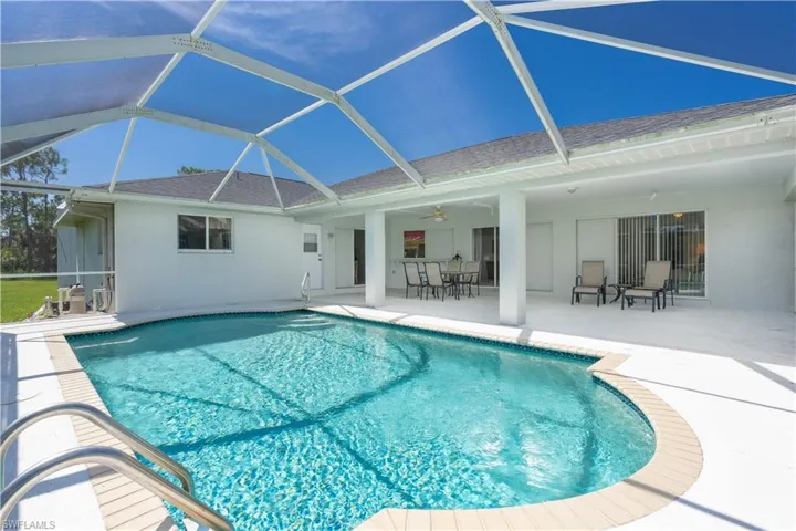View of pool with glass enclosure, ceiling fan, and a patio