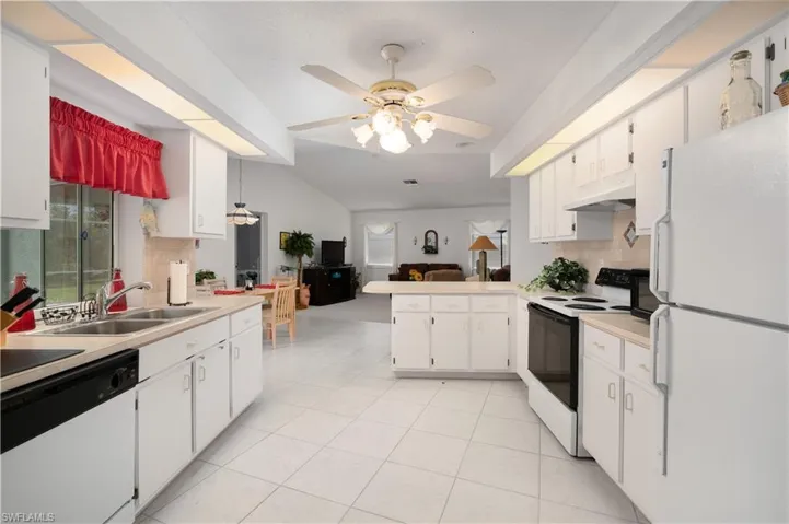 Kitchen featuring ceiling fan, white appliances, decorative backsplash, and white cabinets