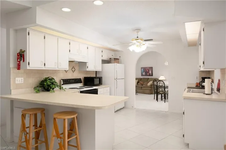 Kitchen featuring ceiling fan, custom range hood, white range with electric cooktop, light tile patterned floors, and tasteful backsplash