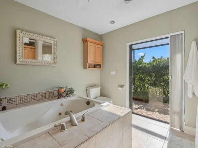 Bathroom with a textured ceiling, a relaxing tiled tub, and toilet