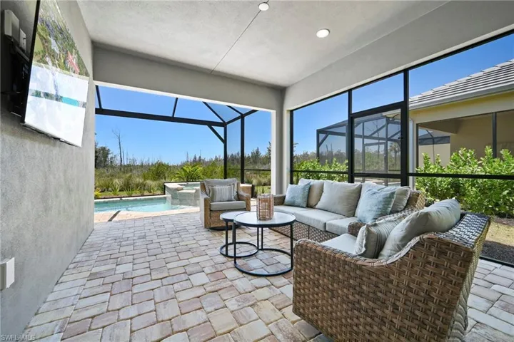 Screened lanai featuring a paver patio, integrated swimming pool with a waterfall feature, and a stucco exterior wall with a mounted television