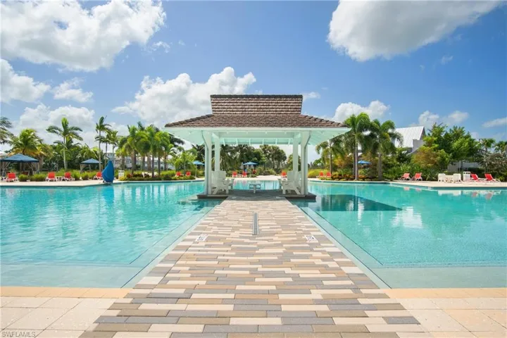 Expansive aquatic amenity featuring a central white gazebo with a shingled roof, surrounded by a large pool with integrated shallow areas