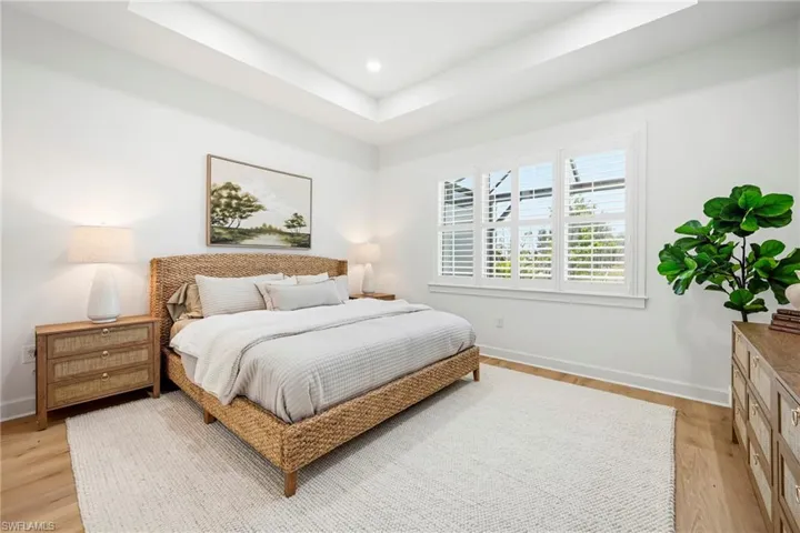 Room featuring wood-finish flooring, a tray ceiling, and multiple windows with plantation shutters