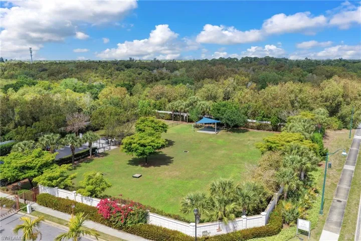 Expansive green space featuring a covered pavilion, mature trees, manicured landscaping, and a surrounding privacy fence