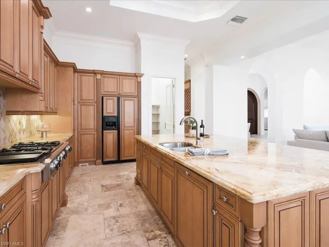 Kitchen with tasteful backsplash, sink, light stone countertops, light tile patterned floors, and a kitchen island with sink
