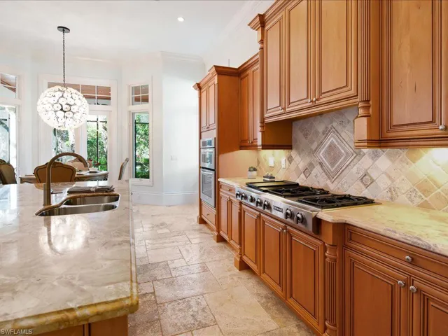 Kitchen featuring decorative light fixtures, decorative backsplash, sink, light stone counters, and appliances with stainless steel finishes