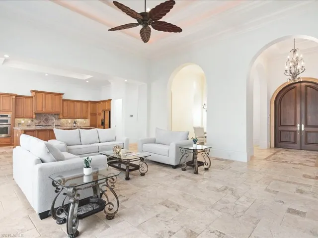 Tiled living room with ceiling fan with notable chandelier, crown molding, and a tray ceiling