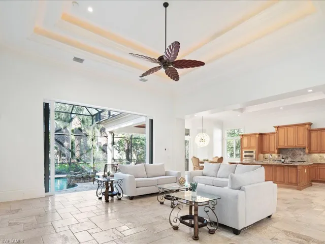 Living room featuring light tile patterned flooring, ceiling fan, a raised ceiling, and crown molding