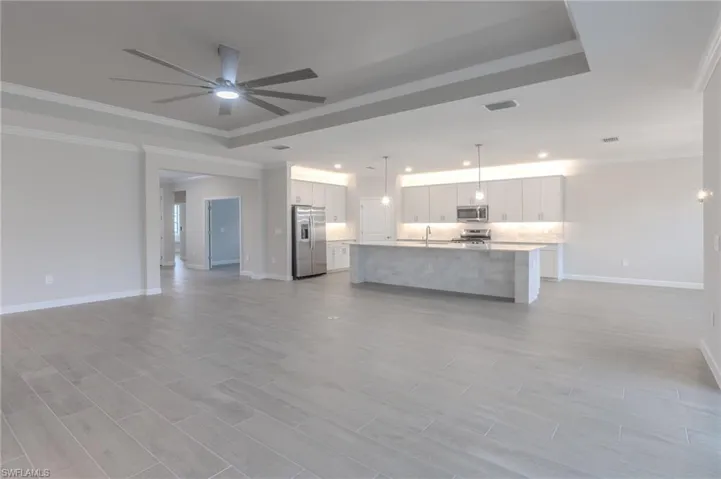 Kitchen featuring stainless steel appliances, backsplash, a center island with sink, ornamental molding, and hanging light fixtures