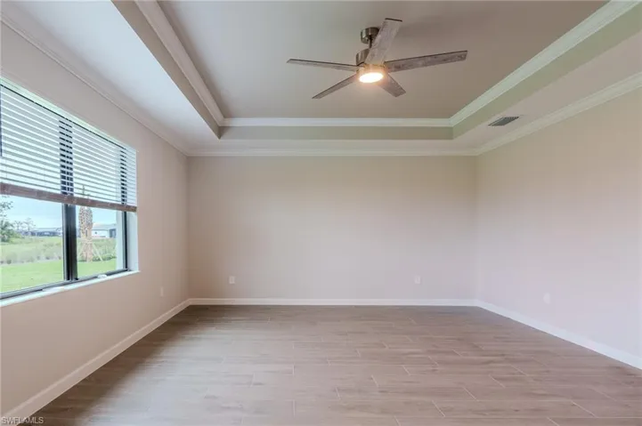Empty room with a ceiling fan, crown molding, light wood-type flooring, and a tray ceiling