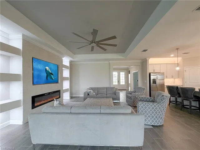 Living area featuring ornamental molding, wood finish floors, a fireplace, ceiling fan, and a raised ceiling