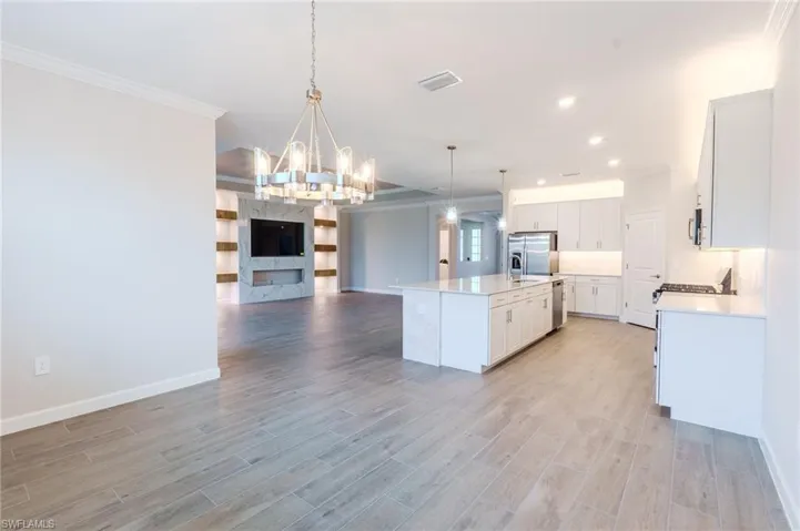 Unfurnished living room featuring ornamental molding, a ceiling fan, a tray ceiling, and light wood finished floors