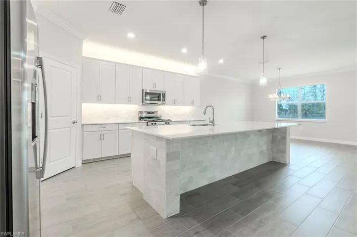 Kitchen featuring stainless steel appliances, an island with sink, backsplash, ornamental molding, and hanging lights