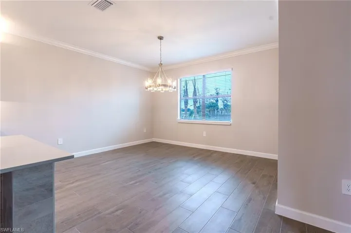 Unfurnished dining area with dark wood finished floors, ornamental molding, and suspended lighting