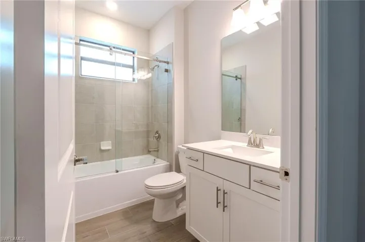 Full bath featuring vanity, enclosed tub / shower combo, and wood finish floors