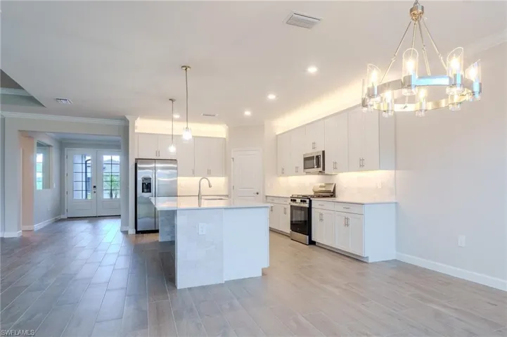 Kitchen featuring open floor plan, suspended lighting, a center island with sink, crown molding, and stainless steel appliances