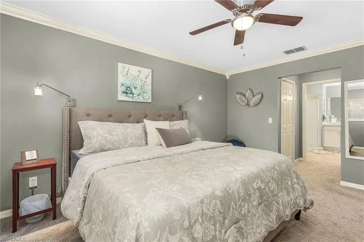 Carpeted bedroom with ornamental molding, a ceiling fan, and ensuite bath