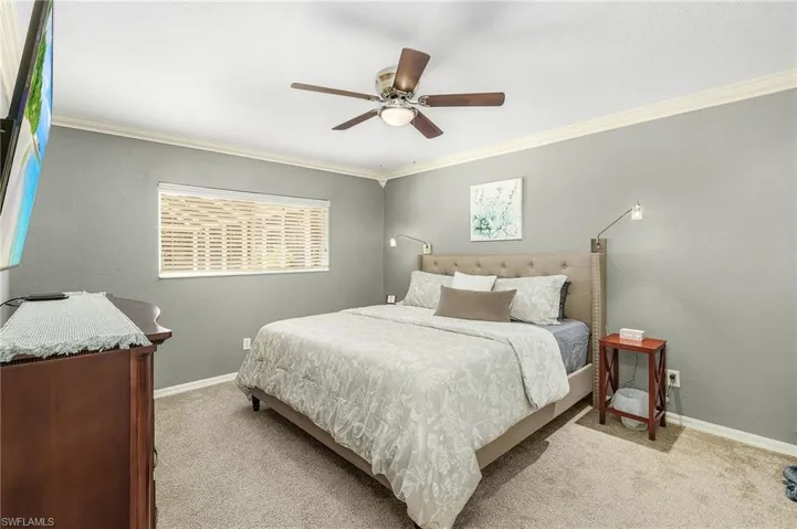 Bedroom with a textured wall, light colored carpet, ornamental molding, and a ceiling fan