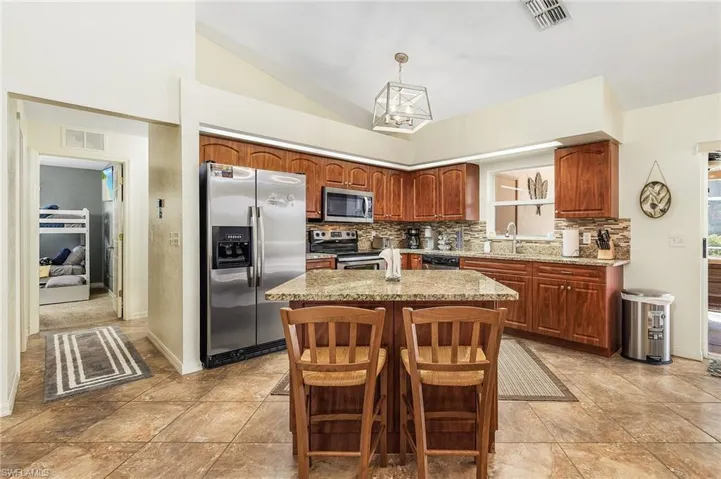Kitchen featuring appliances with stainless steel finishes, brown cabinets, vaulted ceiling, pendant lighting, and a center island