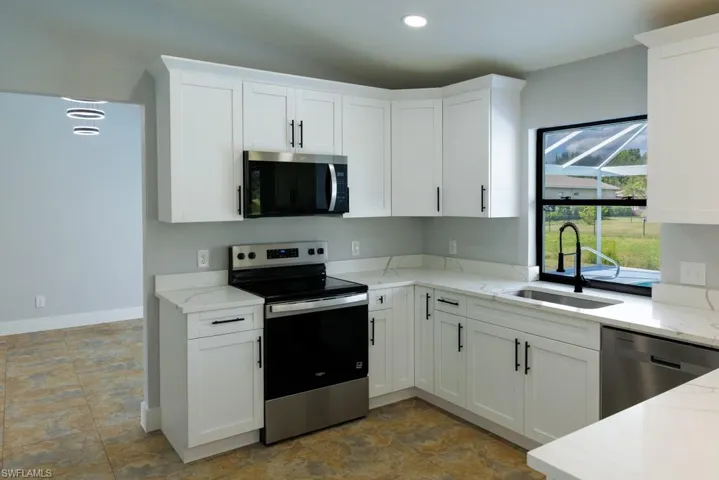 Modern kitchen featuring stainless steel appliances, light stone countertops, white cabinetry, and recessed lighting