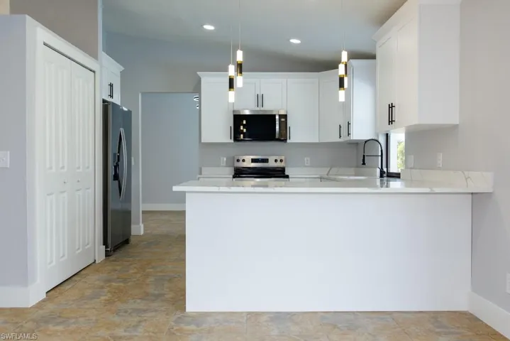 Contemporary kitchen featuring a peninsula, stainless steel appliances, decorative lighting, white cabinetry, and light stone countertops.