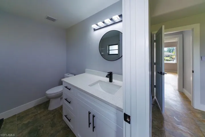 Bright ensuite bathroom with modern finishes, featuring a sleek white vanity, black fixtures, and a contemporary round mirror, a stylish complement to the second master suite