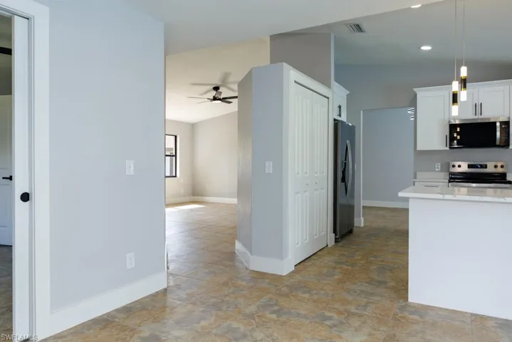 Modern kitchen featuring stainless steel appliances, white cabinetry, pendant lighting, ceiling fan, and light stone countertops.