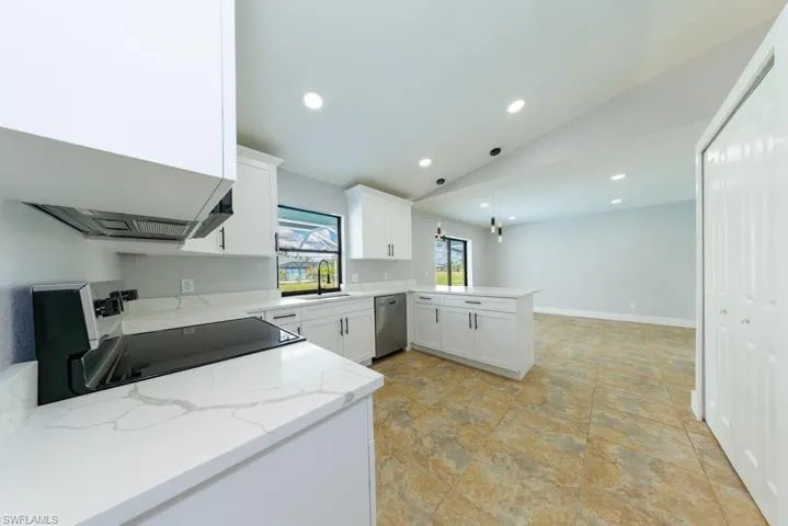 Bright kitchen featuring an electric range, pendant lighting, white cabinetry, and light stone countertops with a peninsula for extra space.