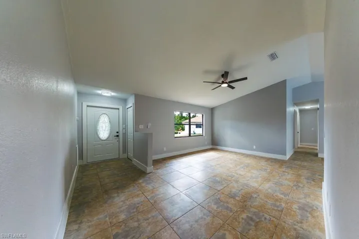 Inviting entryway and living room featuring vaulted ceiling, ceiling fan, and textured walls.