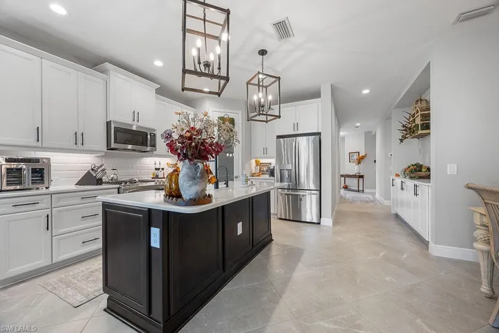 Kitchen with a kitchen island with sink, backsplash, hanging light fixtures, stainless steel appliances, and white cabinetry