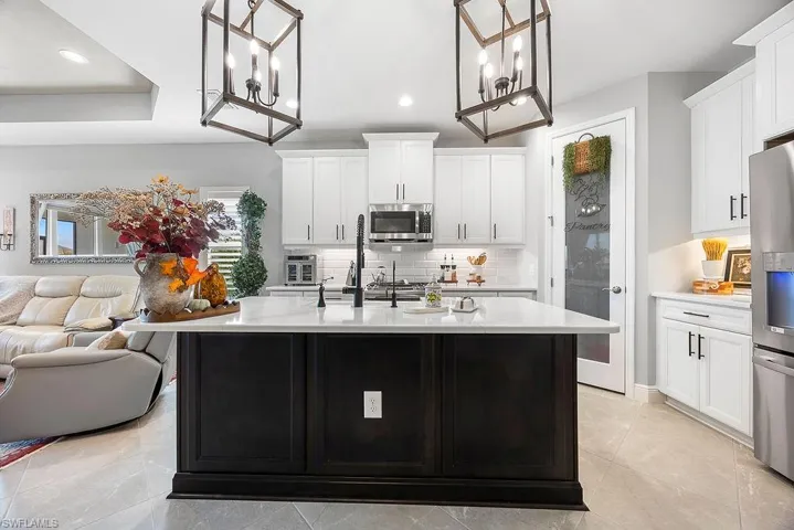 Kitchen with hanging light fixtures, decorative backsplash, white cabinets, stainless steel appliances, and a kitchen island with sink