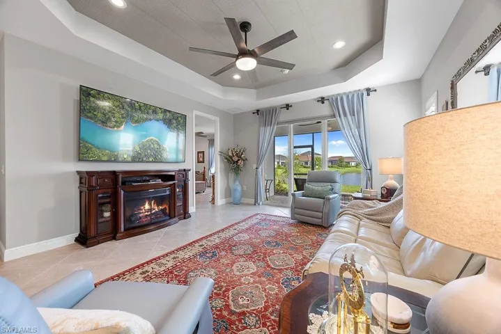Living room featuring a tray ceiling, a glass covered fireplace, recessed lighting, and a ceiling fan