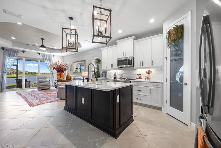 Kitchen featuring stainless steel appliances, white cabinets, a kitchen island with sink, backsplash, and a raised ceiling