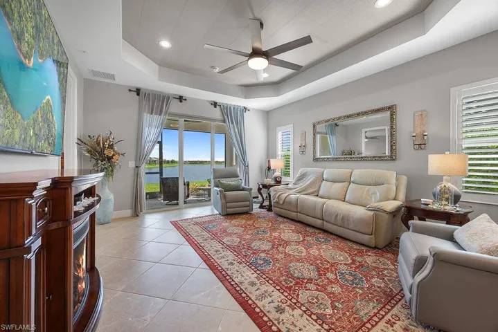 Living room with light tile patterned floors, a ceiling fan, a raised ceiling, recessed lighting, and plenty of natural light