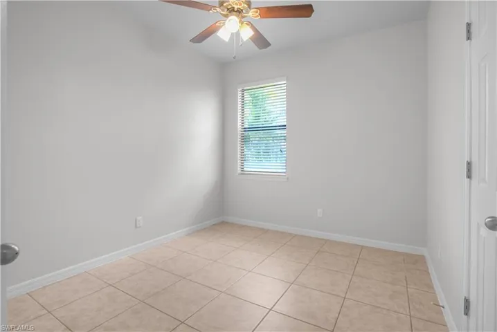 Neutral-toned room featuring tile flooring, a window with horizontal blinds, and a ceiling fan with integrated lighting