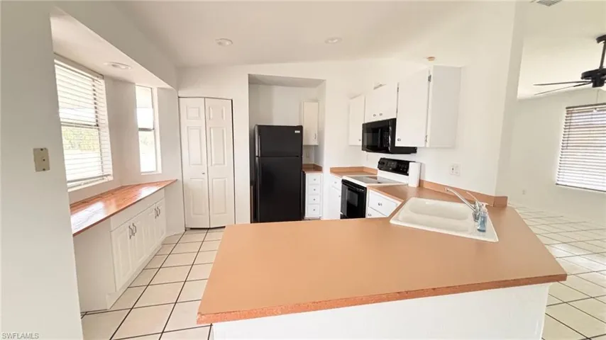 Kitchen featuring white cabinets, black appliances, a peninsula, light tile patterned flooring, and recessed lighting