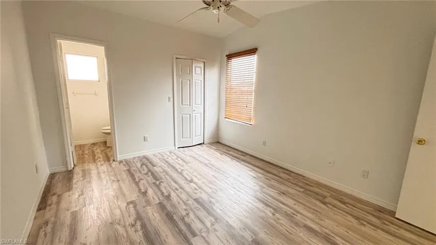 Unfurnished bedroom featuring multiple windows, light wood-style flooring, a ceiling fan, and connected bathroom