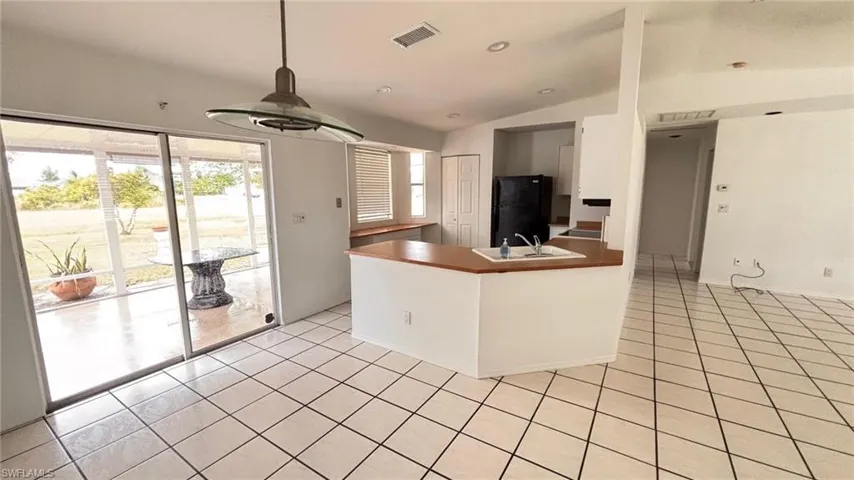 Kitchen with vaulted ceiling, a peninsula, light tile patterned floors, freestanding refrigerator, and hanging light fixtures