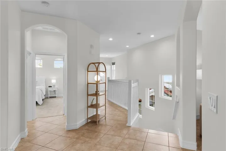 Hall with arched walkways, upstairs landing, tile flooring, and recessed lighting.