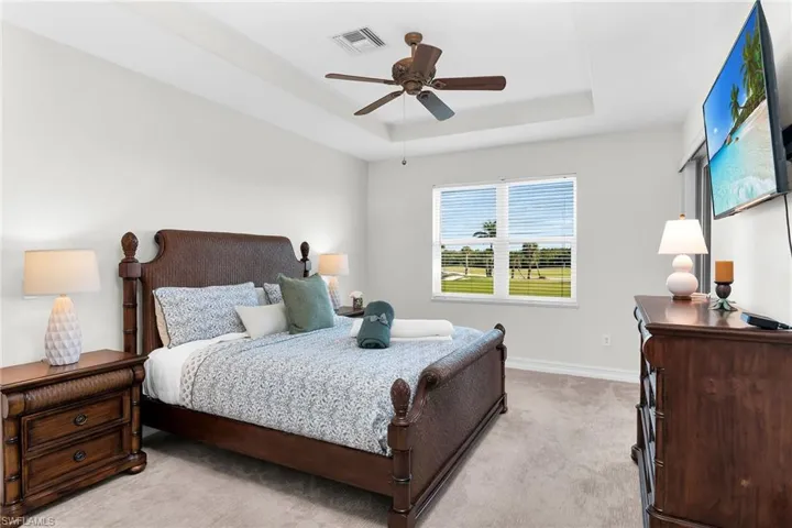 Primary bedroom with tray ceiling, ceiling fan, light-colored carpet, and private lanai access overlooking the golf course.
