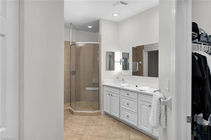 Primary bathroom with stall shower, double vanity, updated cabinetry, new white quartz countertops, tile flooring, and recessed lighting.