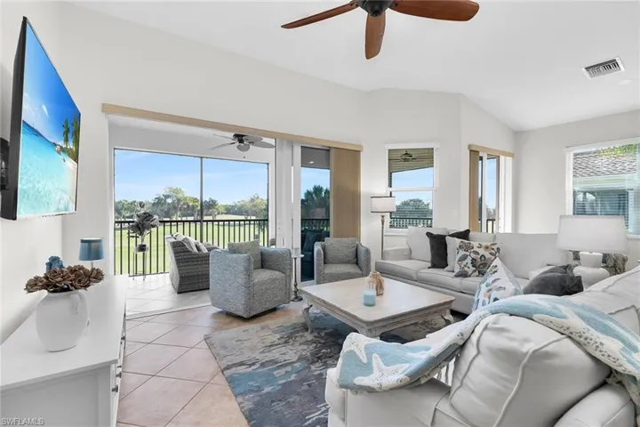 Spacious living area featuring vaulted ceilings, neutral finishes, ceiling fan, and sliding glass doors opening to the lanai with peaceful views.