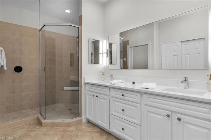 Primary bathroom with stall shower, double vanity, updated cabinetry, new white quartz countertops, tile flooring, and recessed lighting.
