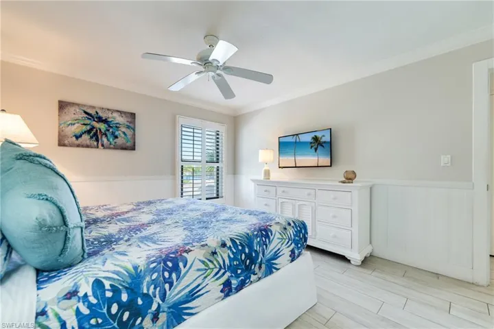 Bedroom featuring a wainscoted wall, crown molding, wood finish floors, and a ceiling fan